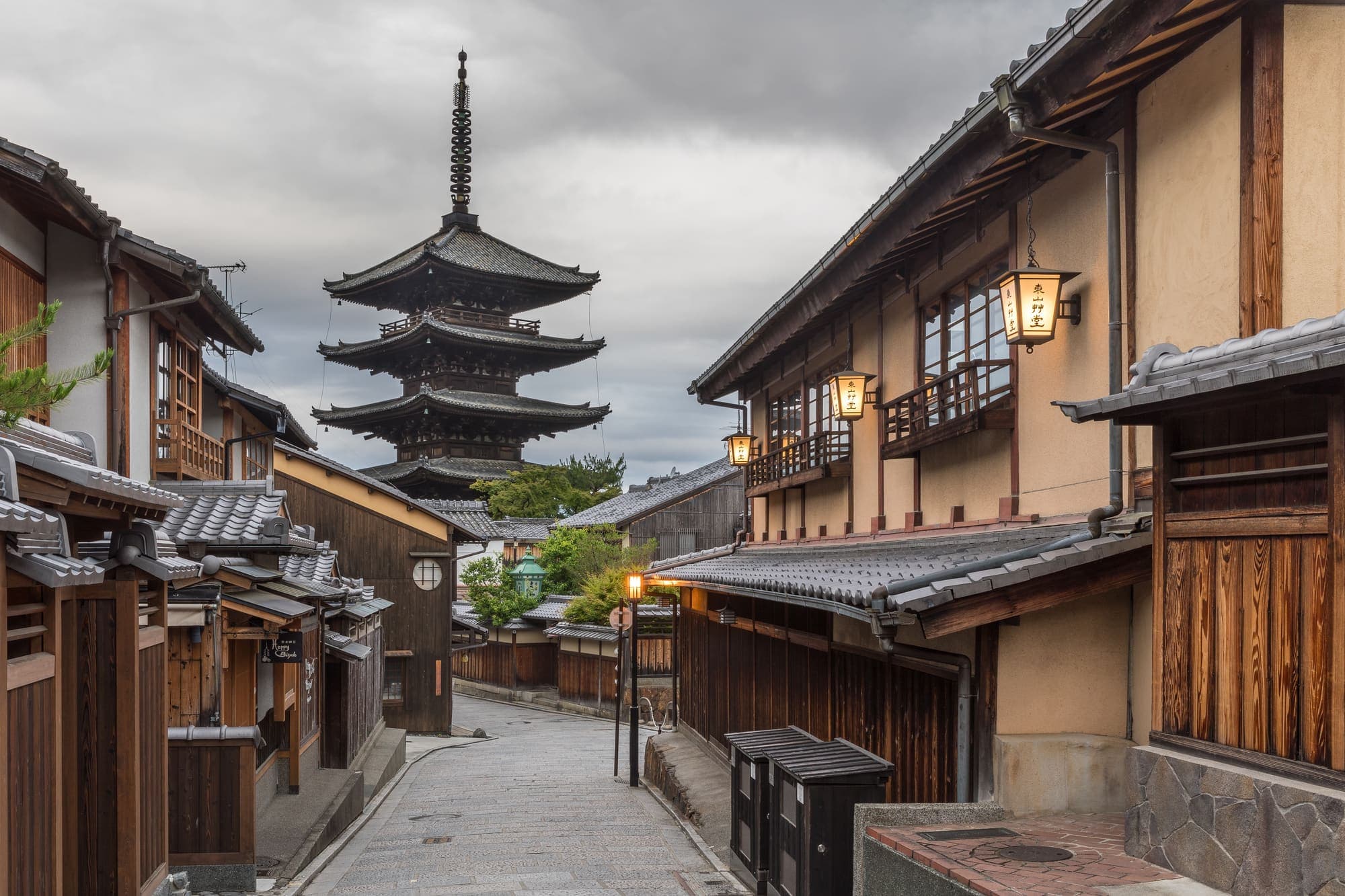 Yasaka-dori in the early morning, with tiled machiya rooftops and street lanterns leading toward the five-storey Yasaka pagoda.
