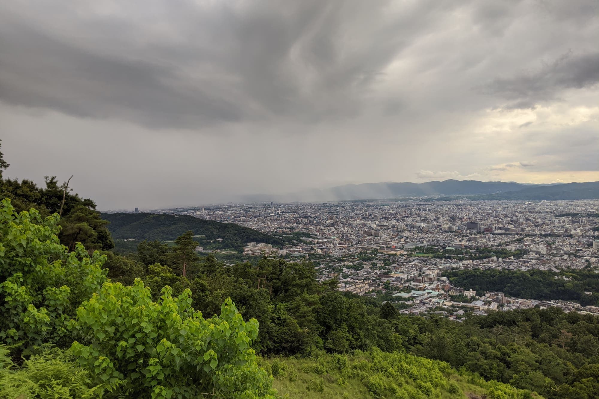The city of Kyoto spread out below the wooded slopes of Mount Daimonji as a rain front moves across the far hills.